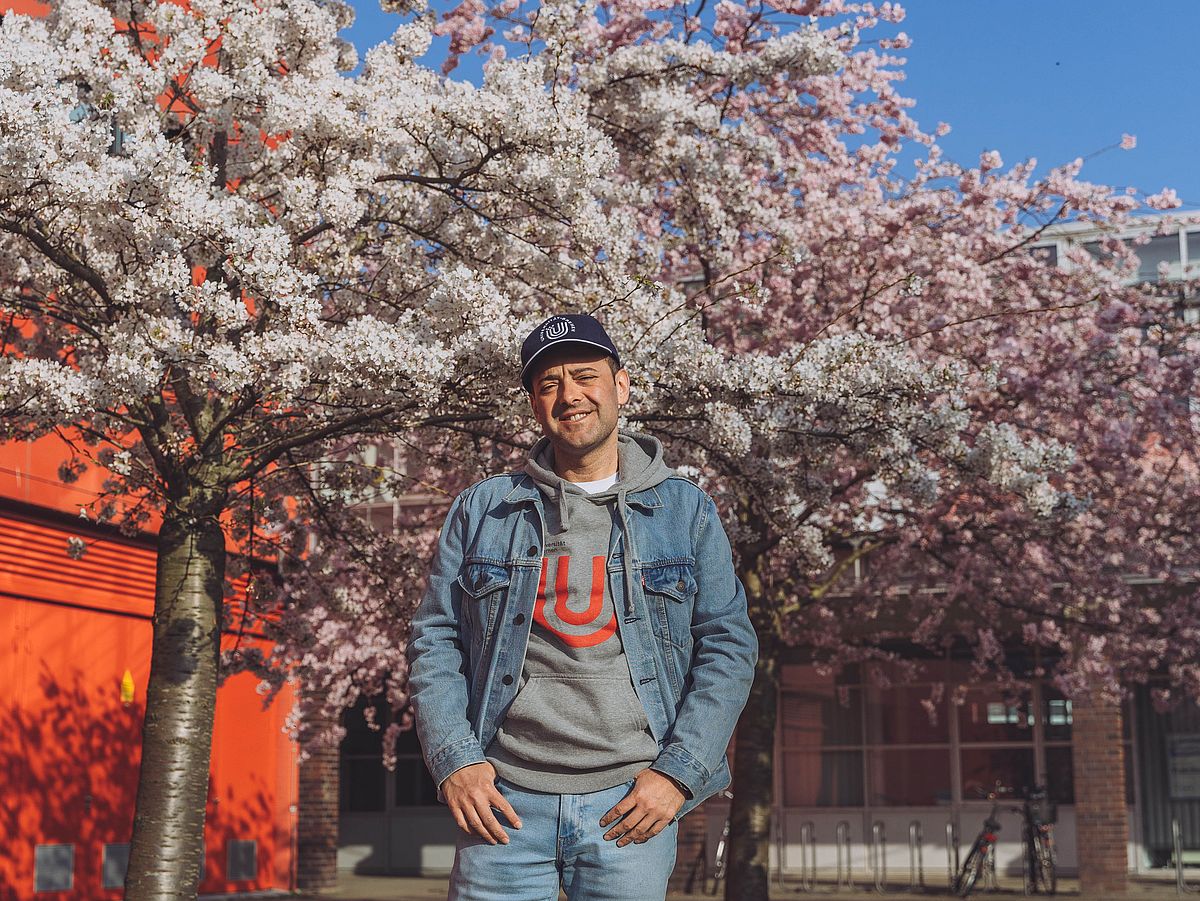 Osman Can Kandemiroglu at the University of Bremen campus in spring, in front of cherry blossoms.